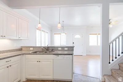 Bright kitchen featuring white cabinetry, a double basin sink, stone-finish countertops, and two pendant lights