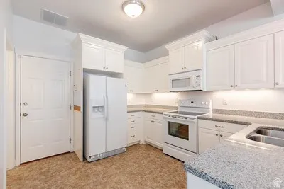Kitchen featuring white cabinetry, white appliances, speckled countertops, stainless steel double basin sink, and wood-finish flooring