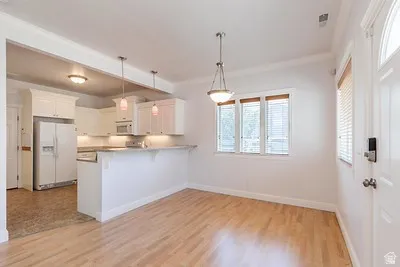 Open-concept living space featuring wood-finish flooring, a contemporary kitchen with white cabinetry, and a peninsula countertop