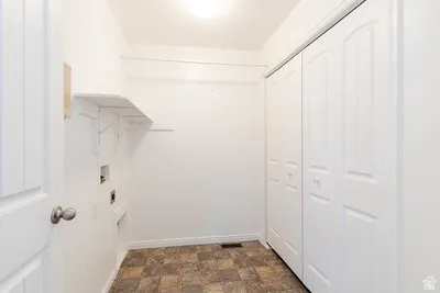 Utility room featuring a tiled floor, white walls, bi-fold closet doors, wall-mounted shelving, and appliance hookups