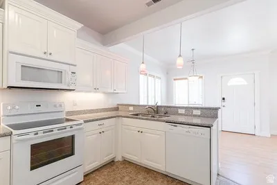 Kitchen featuring white cabinetry, stone-finish countertops, stainless steel sink, and white appliances
