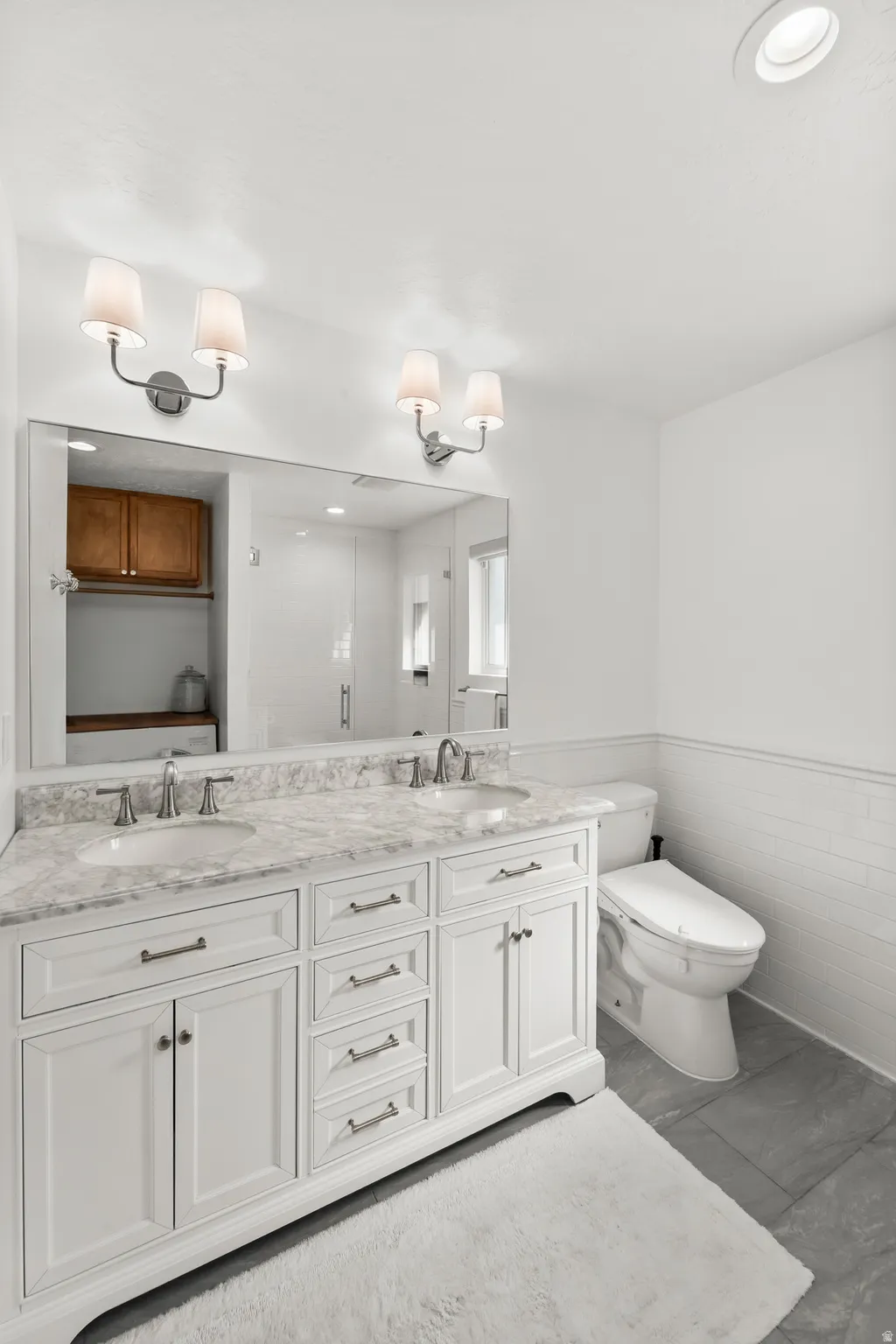 Spacious bathroom featuring a dual vanity with a stone-finish countertop, white cabinetry, and brushed nickel hardware