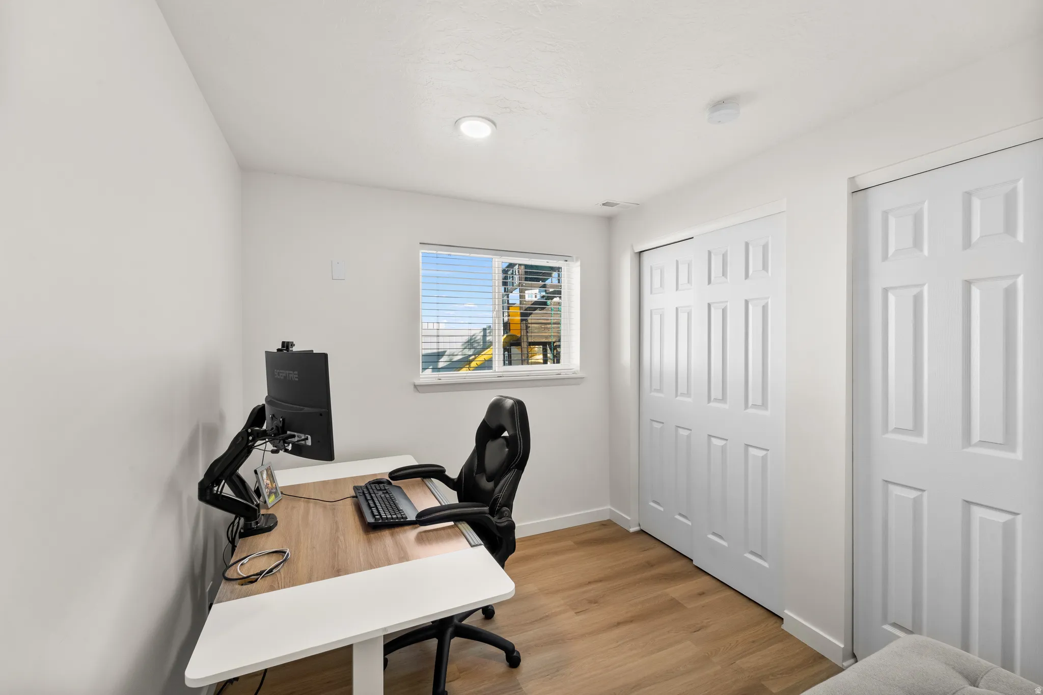 Room featuring light wood-finish flooring, white walls, and a window with horizontal blinds