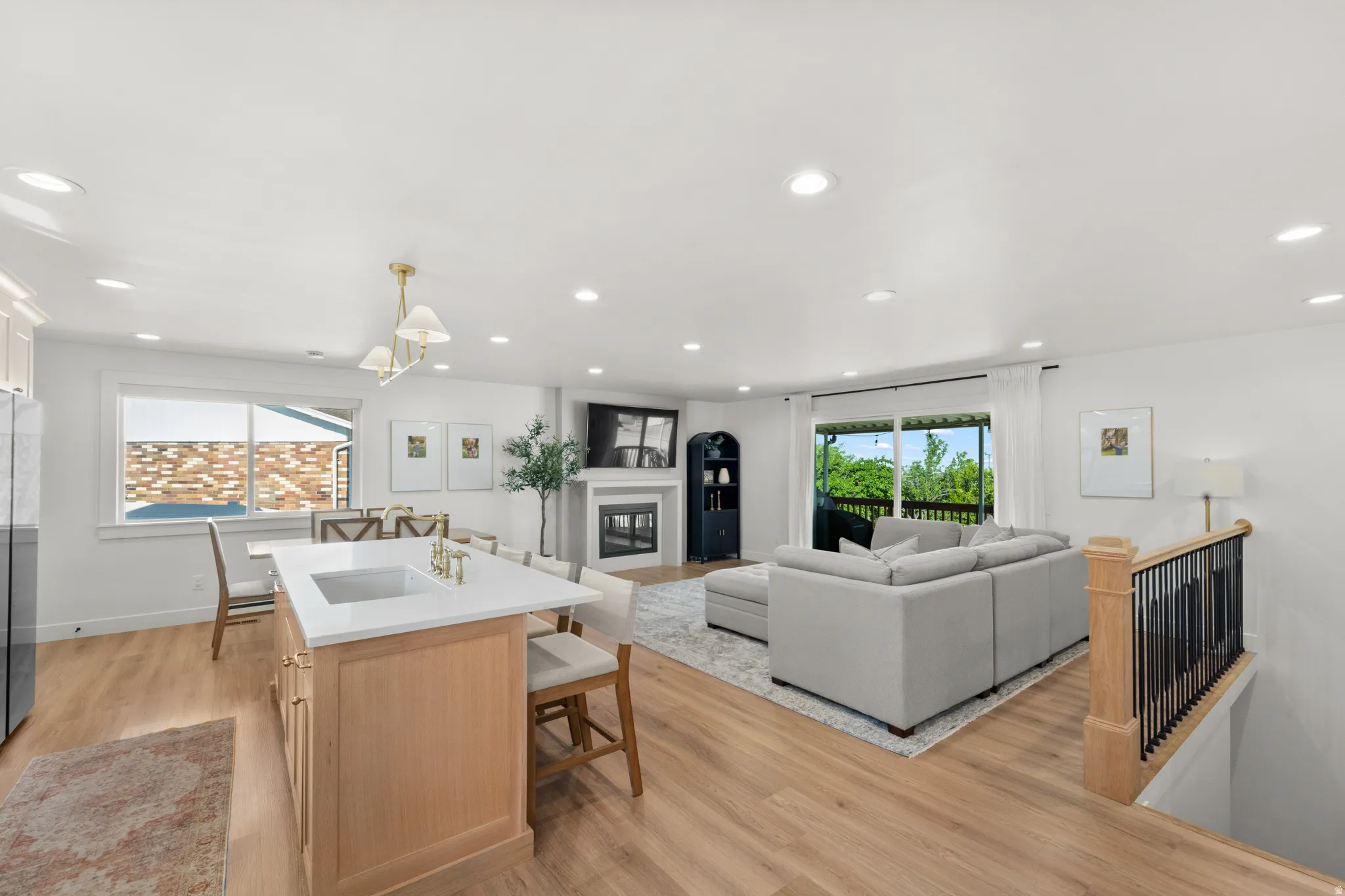 Open-concept living area featuring wood-finish flooring, recessed lighting, and a kitchen island with a built-in sink and gold-tone faucet