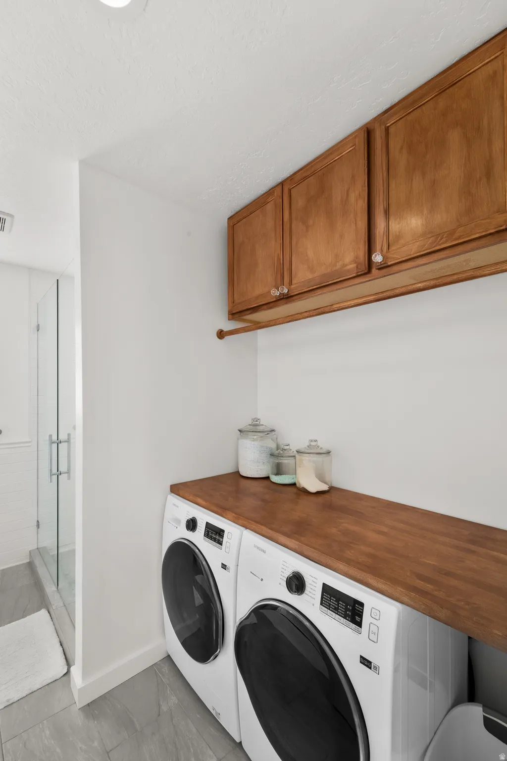 Laundry area featuring stacked front-loading appliances, a wood-finish countertop, and overhead wood cabinetry with clear knob hardware
