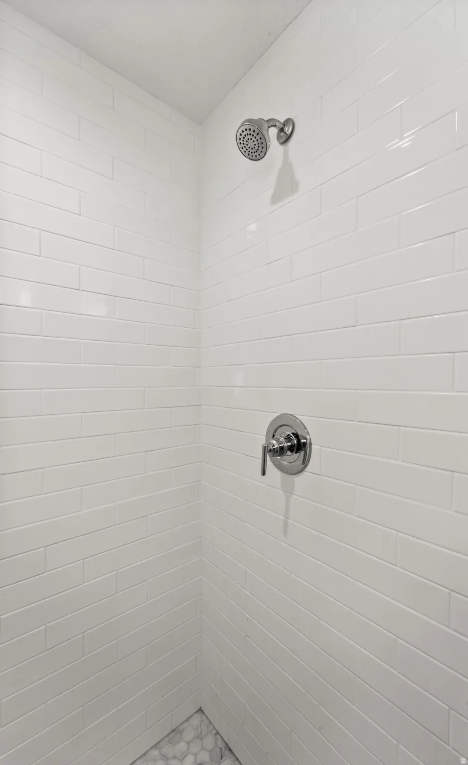 Shower featuring white subway tile walls, a chrome shower head, a chrome single-handle control, and a pebble tile floor