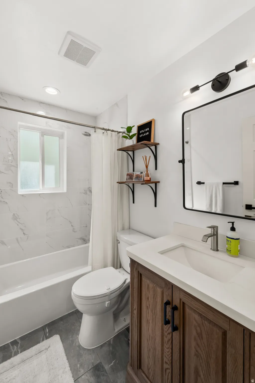 Full bathroom with a white bathtub and shower featuring white and gray marble-look tile