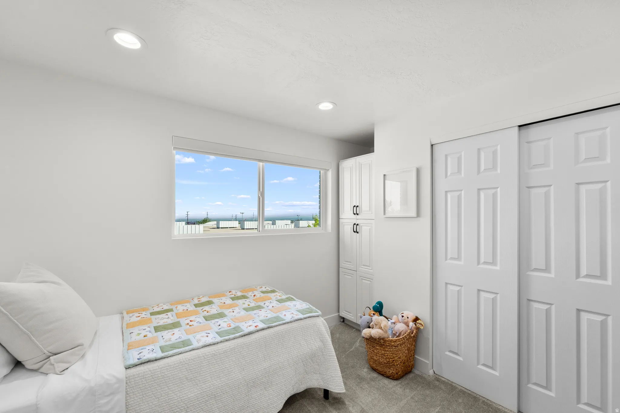 Interior room featuring a large window, integrated overhead lighting, built-in cabinetry with dark hardware, sliding panel doors, and grey carpet flooring