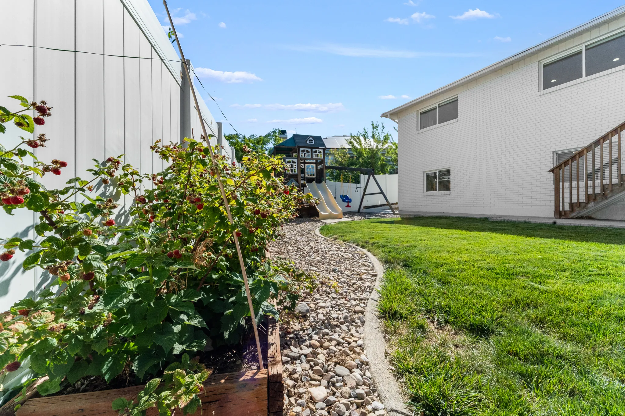 Expansive backyard featuring a green lawn, curved rock garden bed, and mature berry bushes