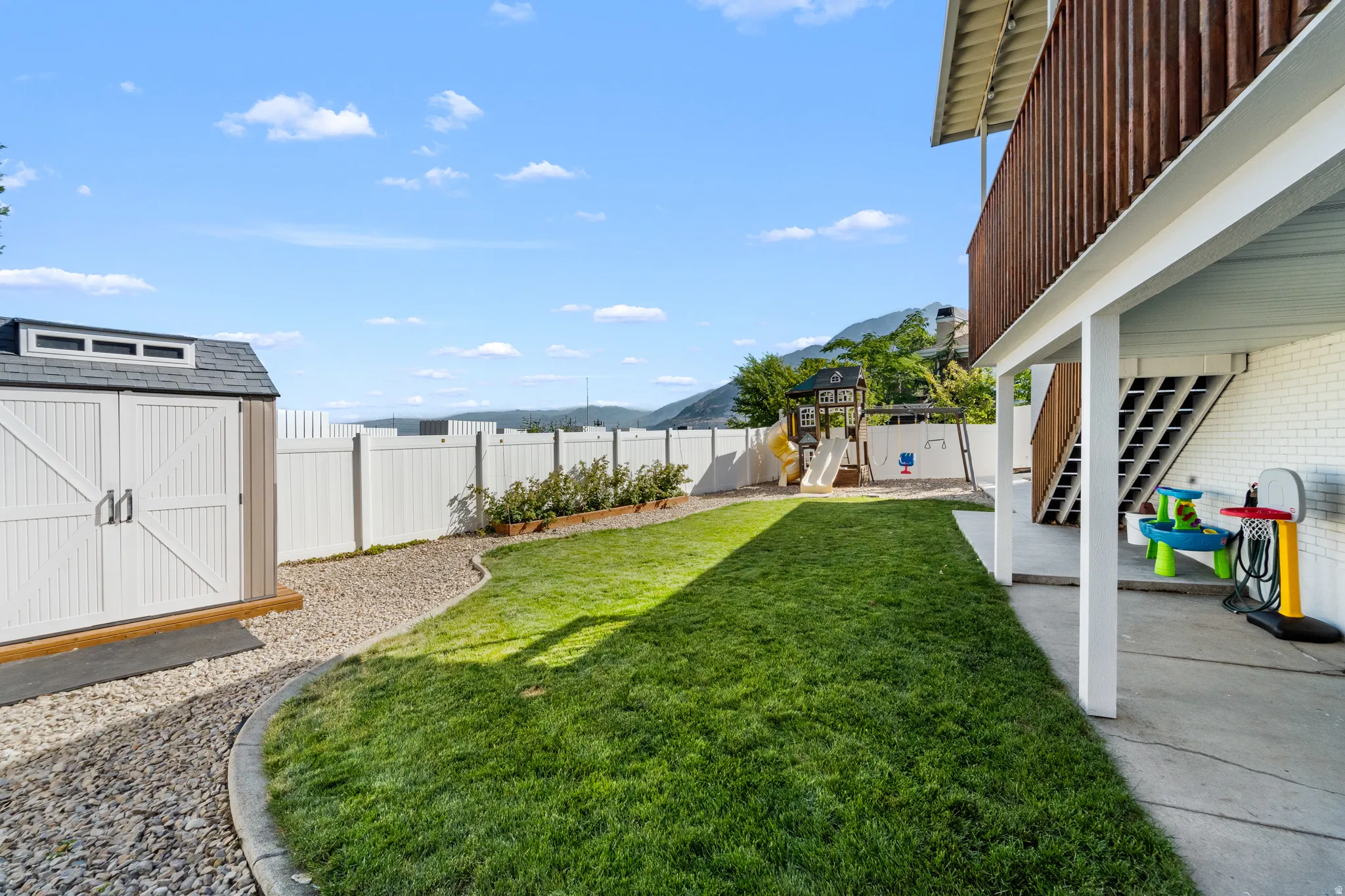 Expansive backyard featuring a lush lawn, white privacy fencing, and a built-in storage shed
