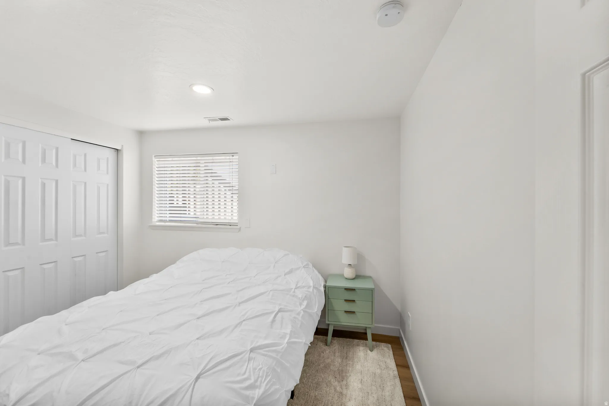 Bright interior space featuring a window with horizontal blinds, recessed lighting, and wood-finish flooring