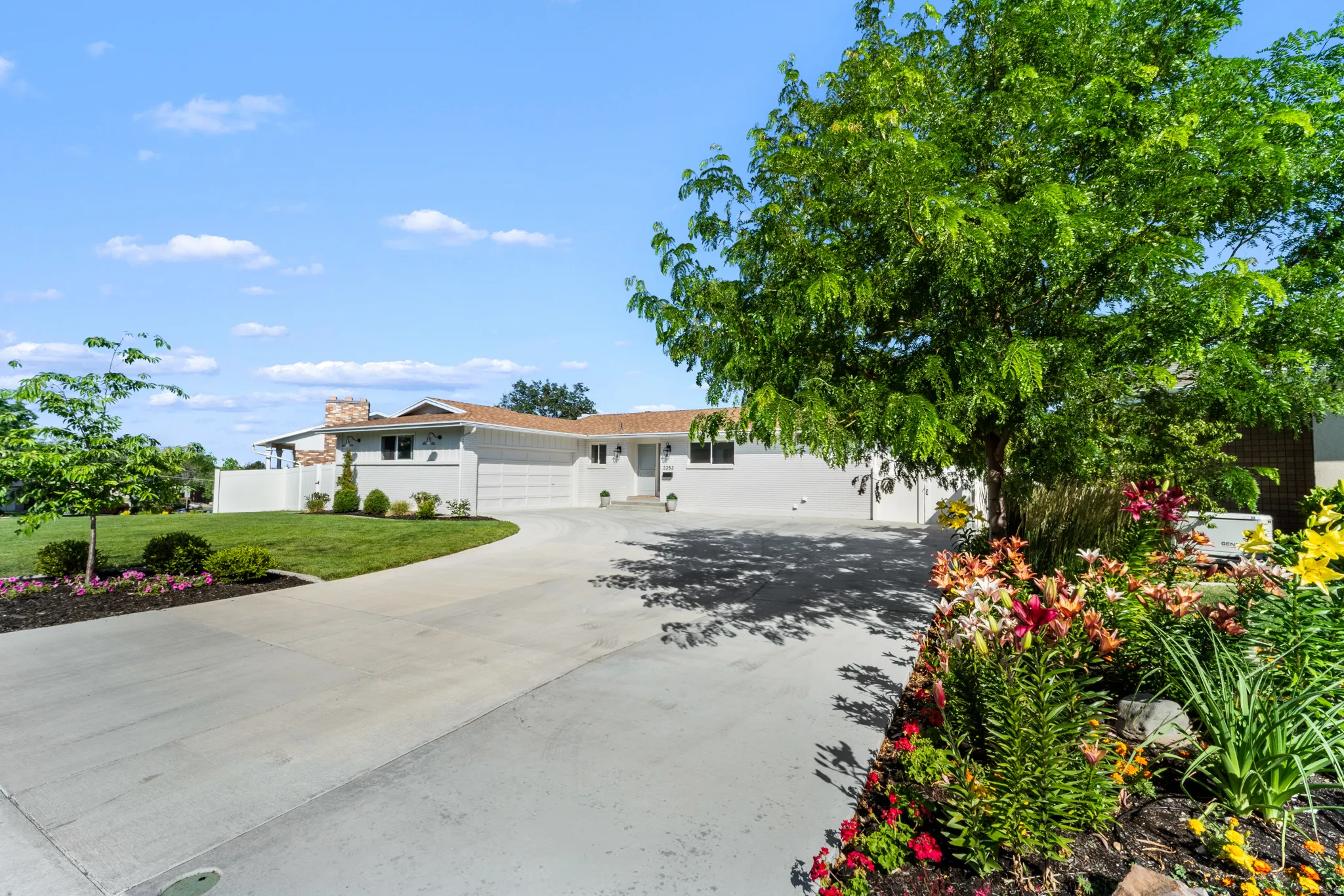Spacious paved driveway leading to a single-story residence with a stone-clad chimney and a two-car garage