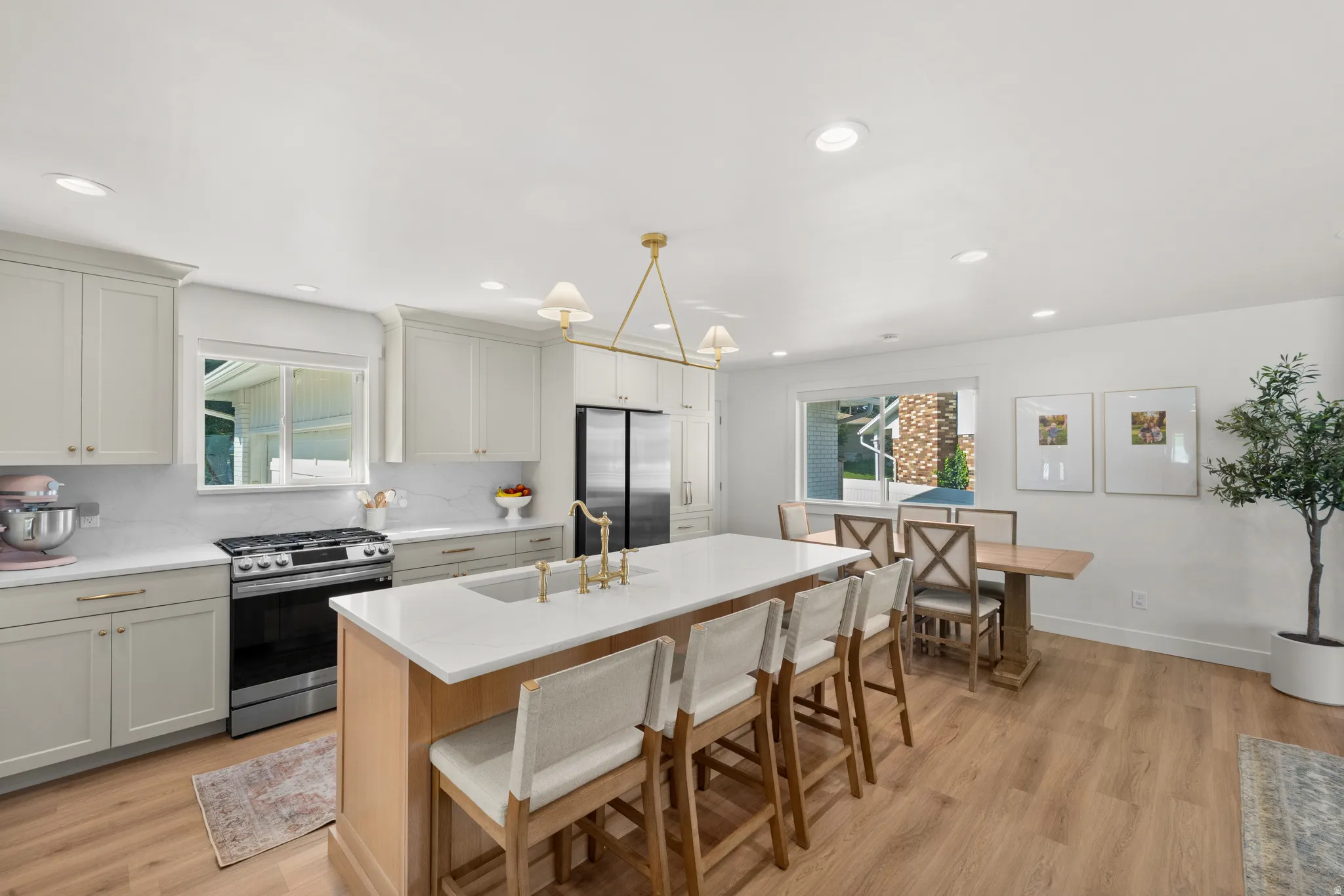 Open-concept kitchen featuring light wood-finish flooring, white cabinetry with gold hardware, a large central island with seating, a stainless steel range, and a dining area