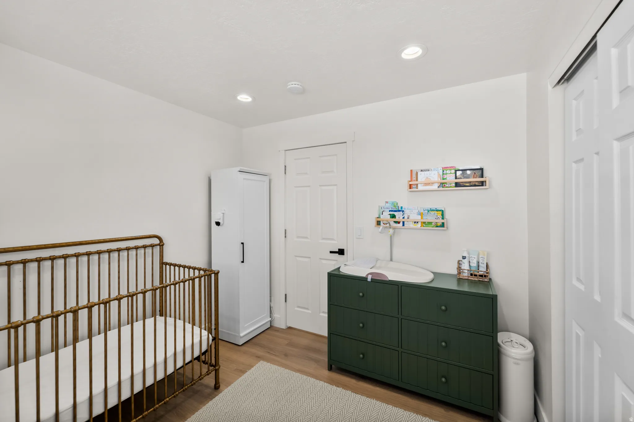 Bright room featuring recessed lighting, wood-finish flooring, white walls, and a white paneled door with black hardware