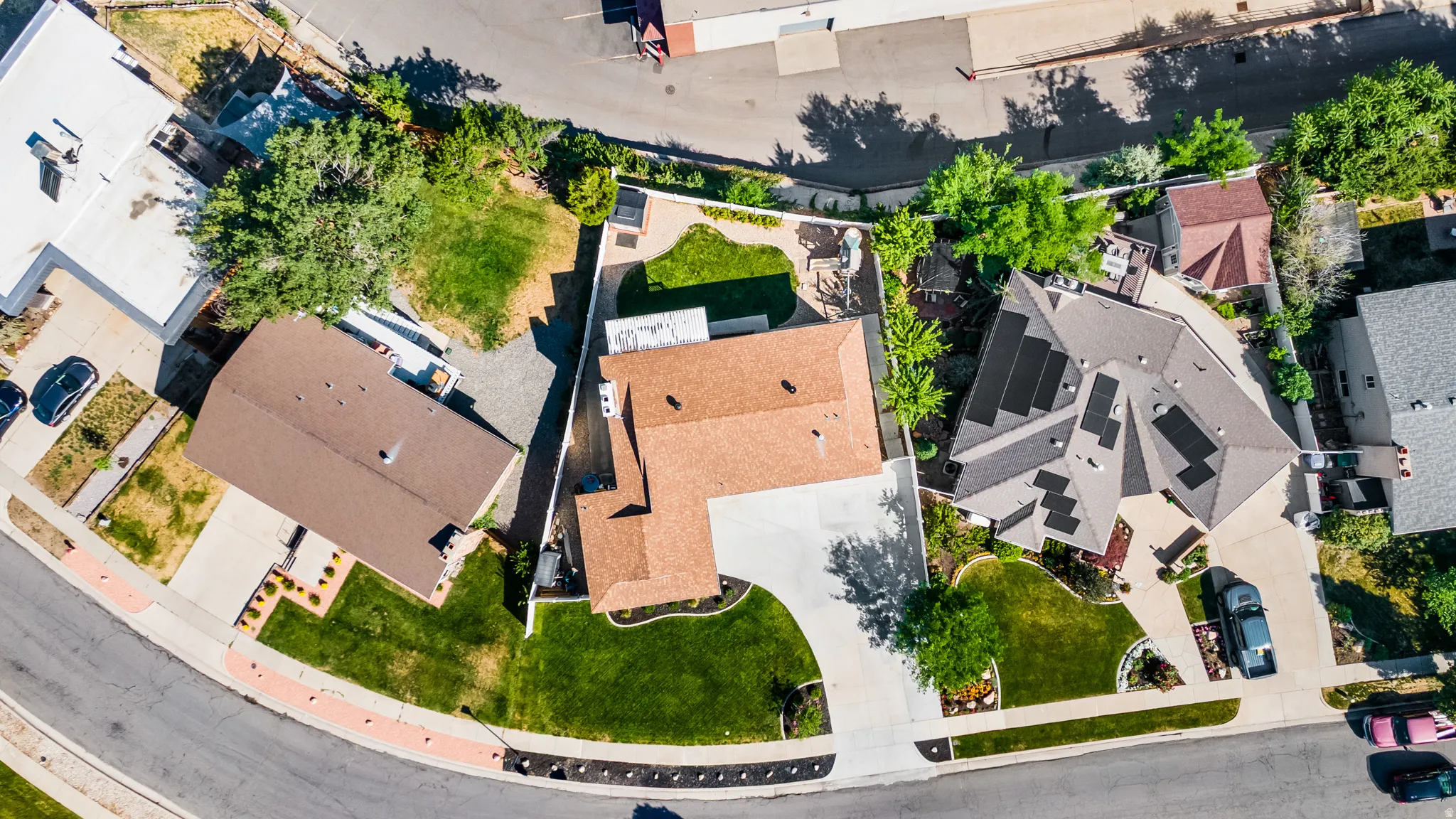 Spacious residential property featuring a large paved driveway, extensive green lawns, mature trees, and a private rear patio area