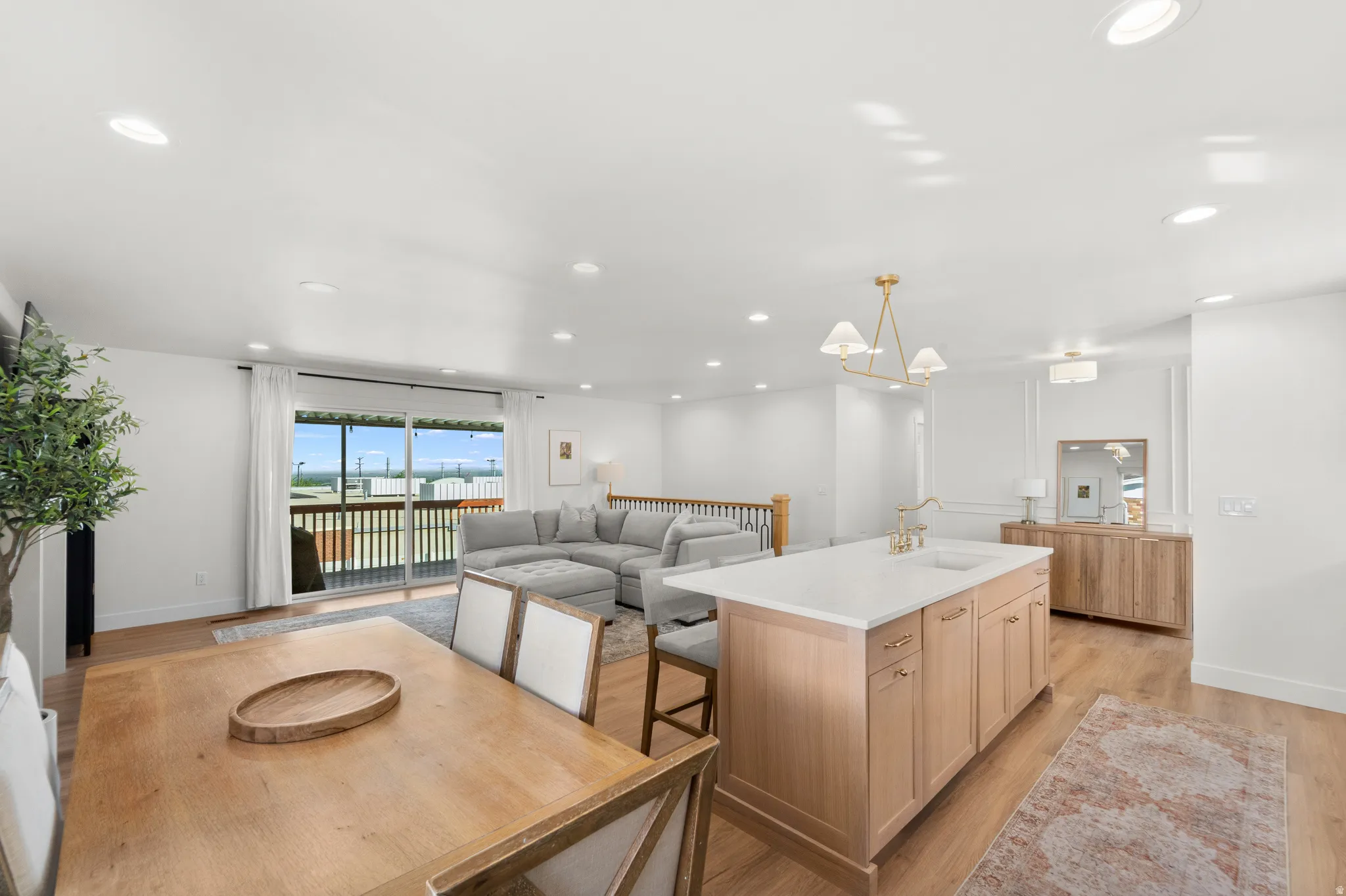 Open-concept living space featuring wood-finish flooring throughout, a central kitchen island with a light-toned countertop, and sliding glass doors opening to an outdoor deck