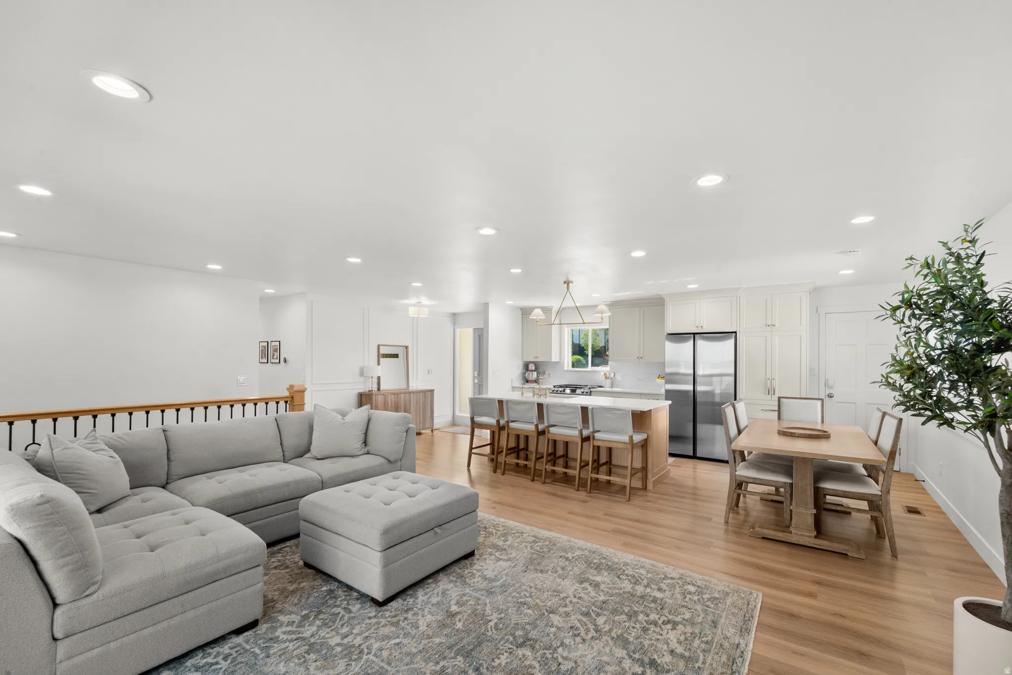 Open-concept living space featuring wood-finish flooring, recessed lighting, and a kitchen with white cabinetry, a center island with seating, and stainless steel appliances