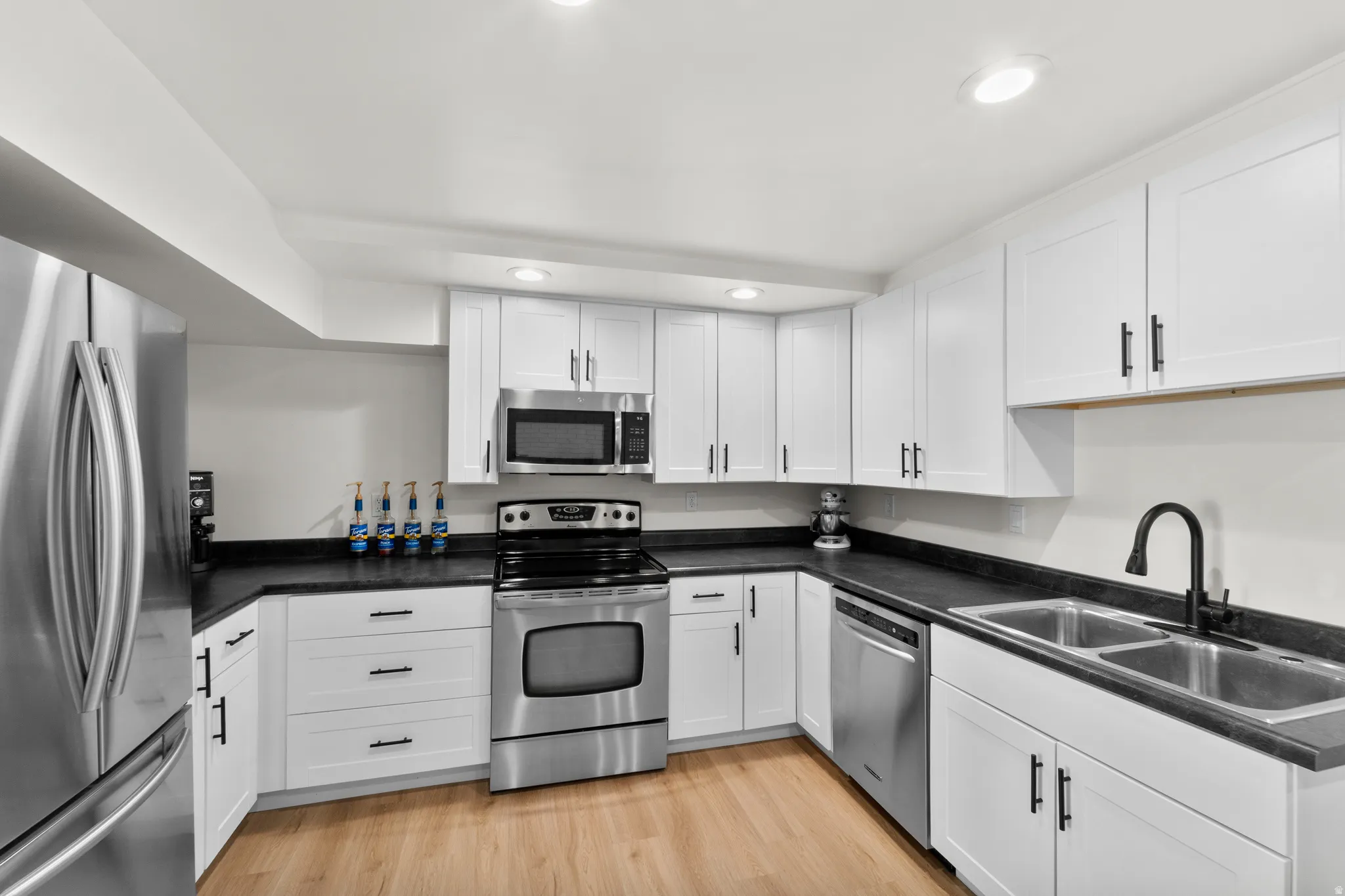 Modern kitchen featuring white shaker cabinetry, stainless steel appliances, dark countertops, and wood-finish flooring