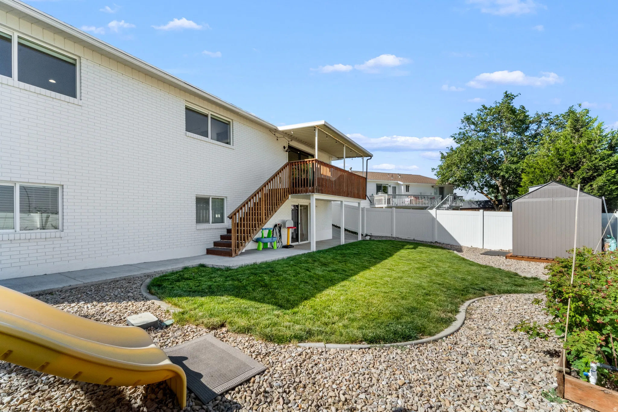 White brick exterior with upper-level deck, lower-level patio, and wood-finish stairway