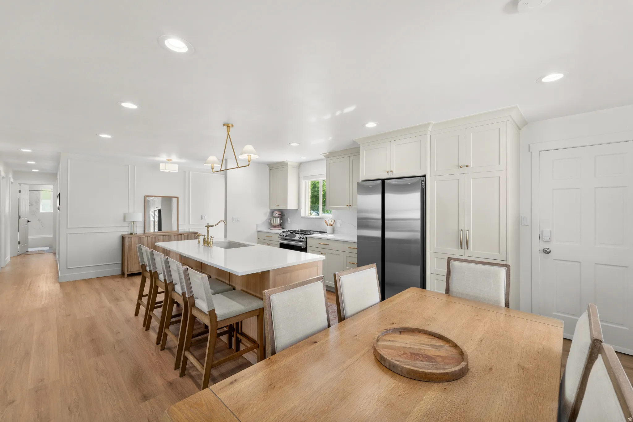 Open-concept kitchen and dining area featuring light wood-finish flooring, a central island with integrated sink, recessed lighting, white perimeter cabinetry, and stainless steel appliances