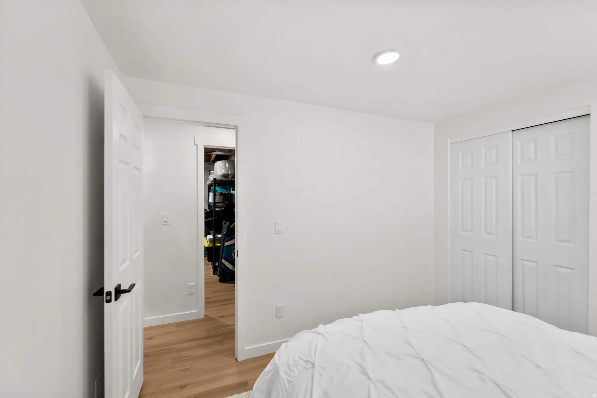 White interior with recessed lighting, wood-finish flooring, a paneled door with black hardware, and a bifold closet door