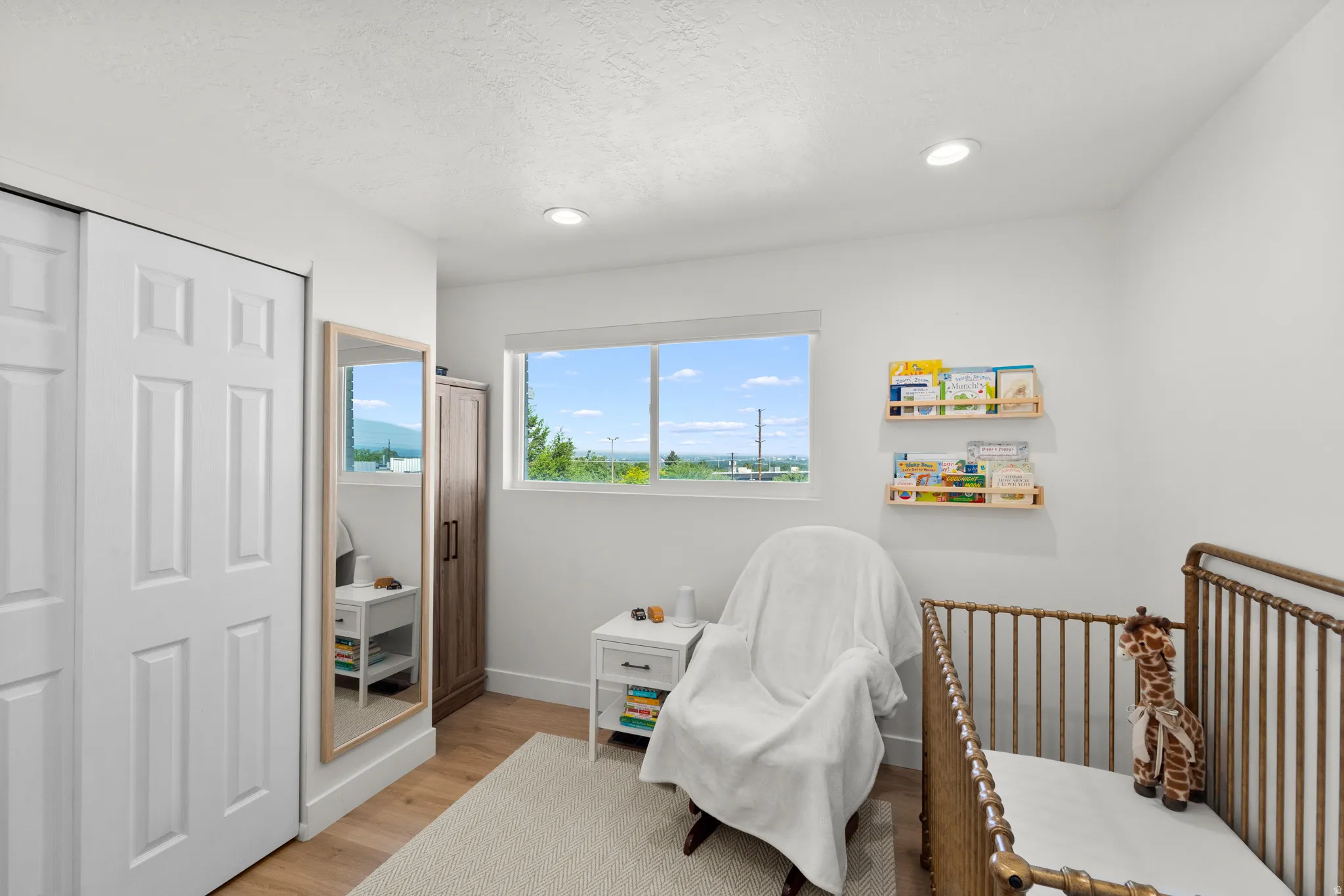 Bright room featuring wood-finish flooring, recessed lighting, white walls, and a window with outdoor scenery