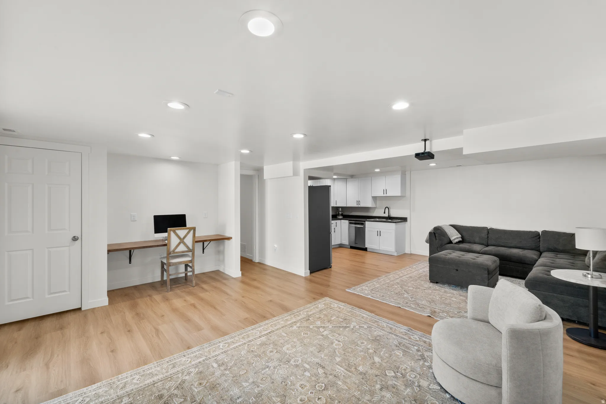 Open-concept living area featuring wood-finish flooring, recessed lighting, and a built-in kitchen space with white cabinetry and dark countertops