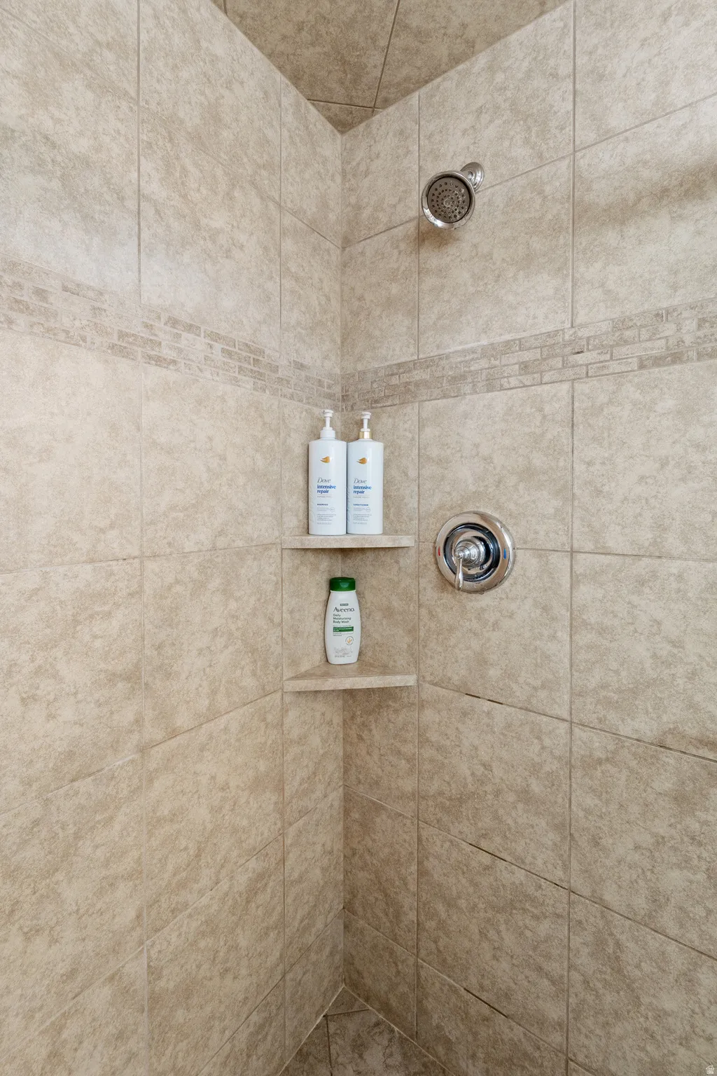 Tiled shower enclosure featuring a mosaic accent band, built-in corner shelving, and chrome fixtures