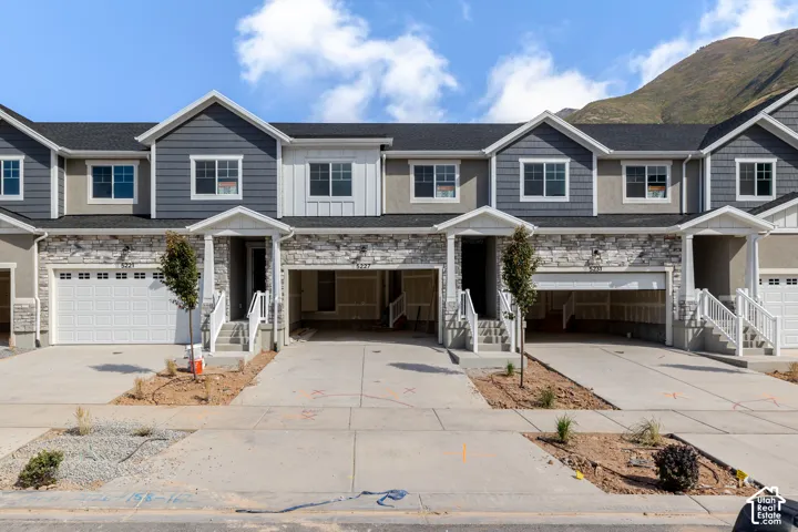 Multi-level townhouse exterior featuring stacked stone veneer, contrasting lap and vertical siding, attached garages, covered entryways, and mountain backdrop