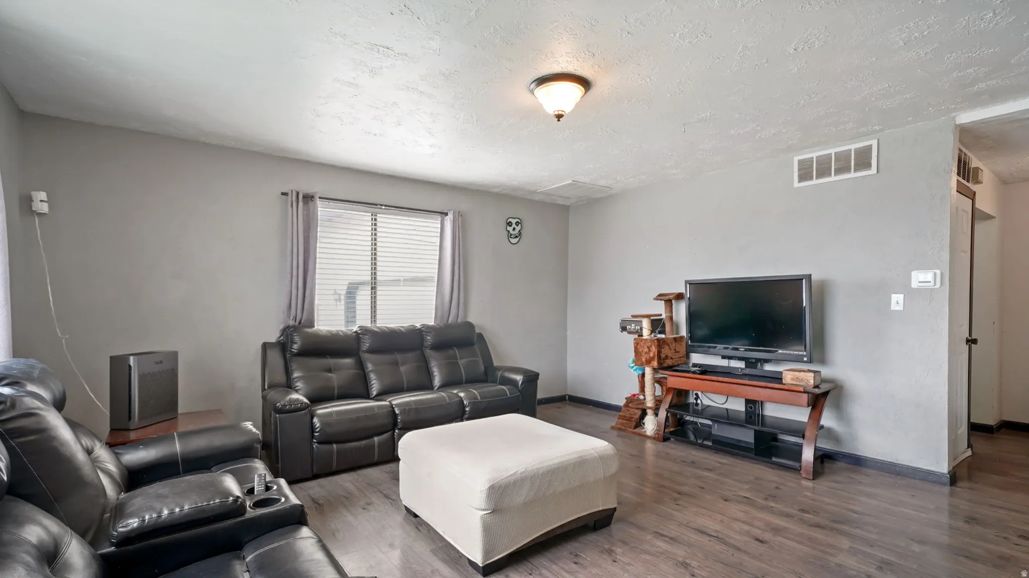 Living area featuring wood-finish flooring, light gray wall paint, and a single window with horizontal blinds