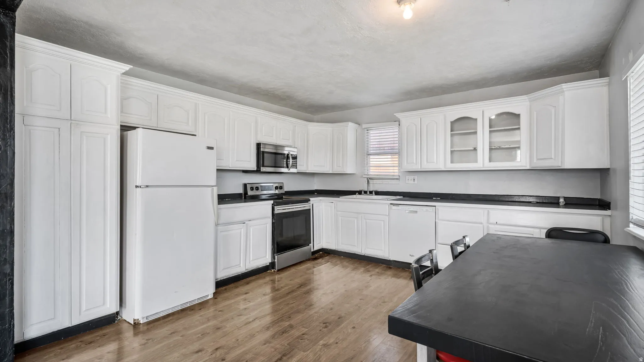Full kitchen featuring white cabinetry, dark countertops, a stainless steel microwave, a stainless steel range, and wood-finish flooring