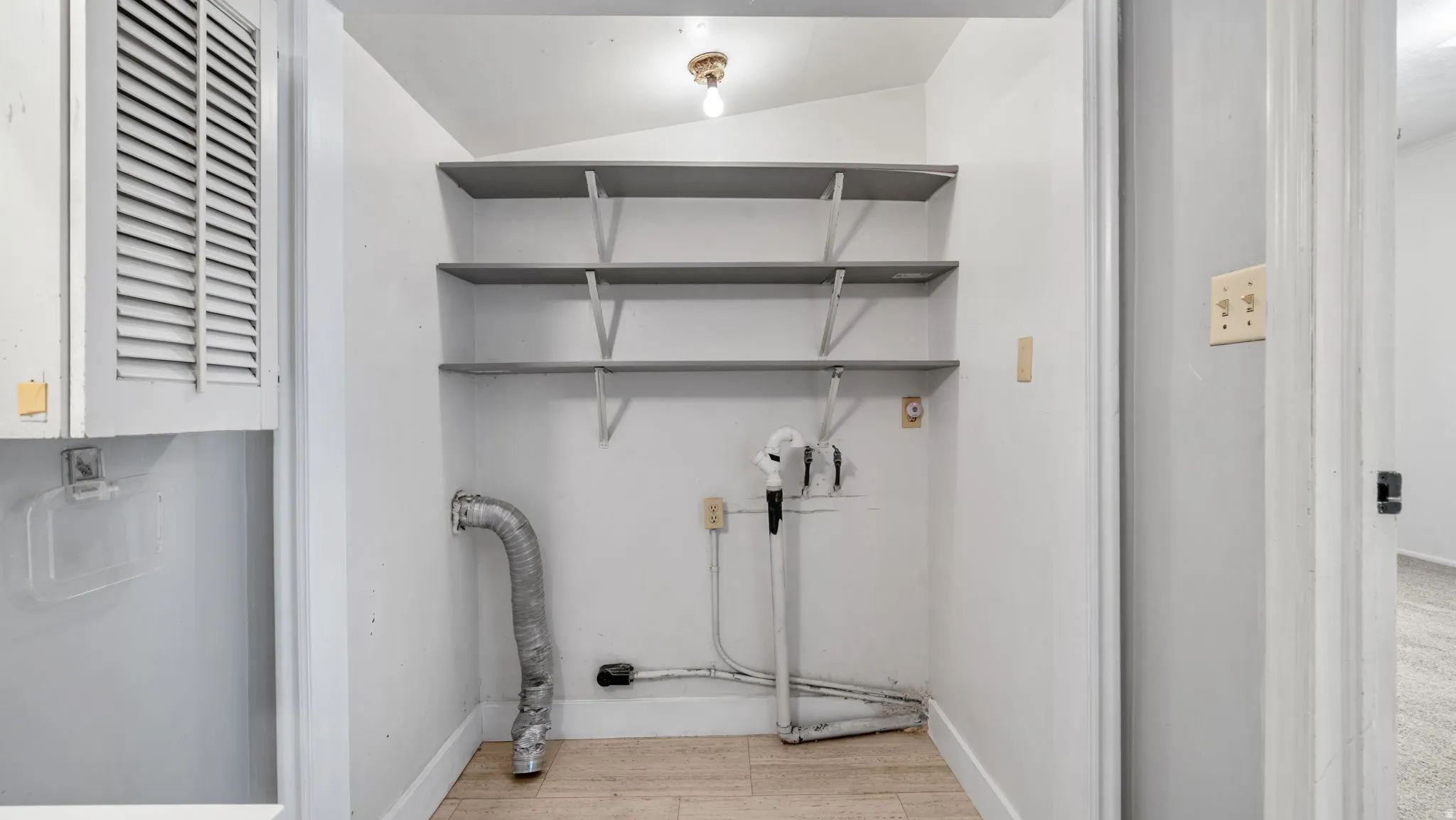 Utility closet with integrated shelving, overhead lighting, and wood-finish flooring
