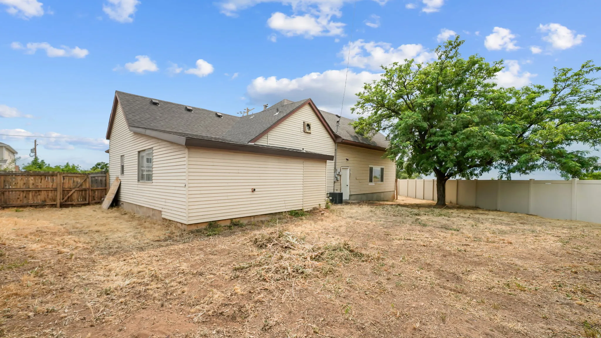 Spacious backyard featuring a large tree, a full privacy fence, and an exterior door