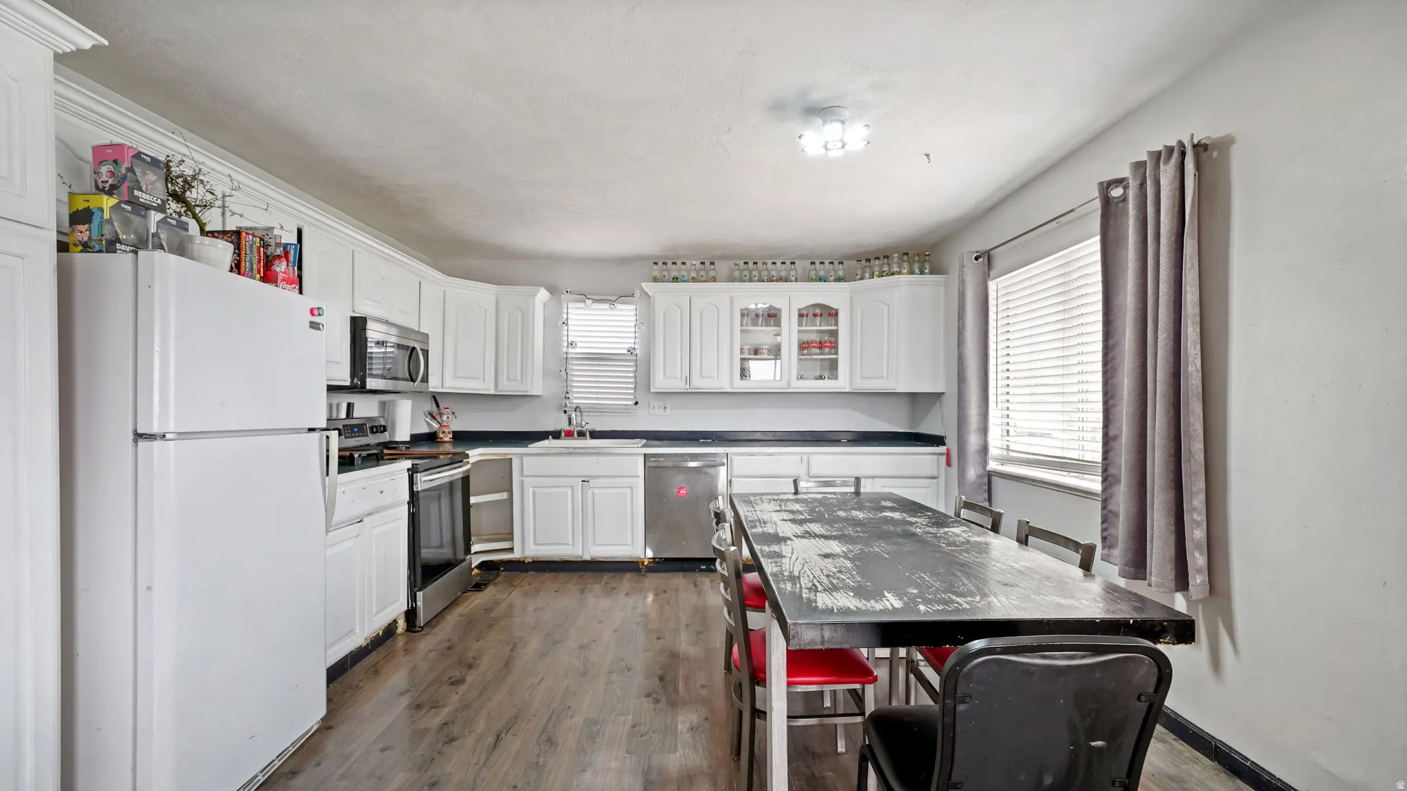 Kitchen featuring white cabinetry, dark countertops, wood-finish flooring, and built-in stainless steel appliances including a microwave, oven, and dishwasher