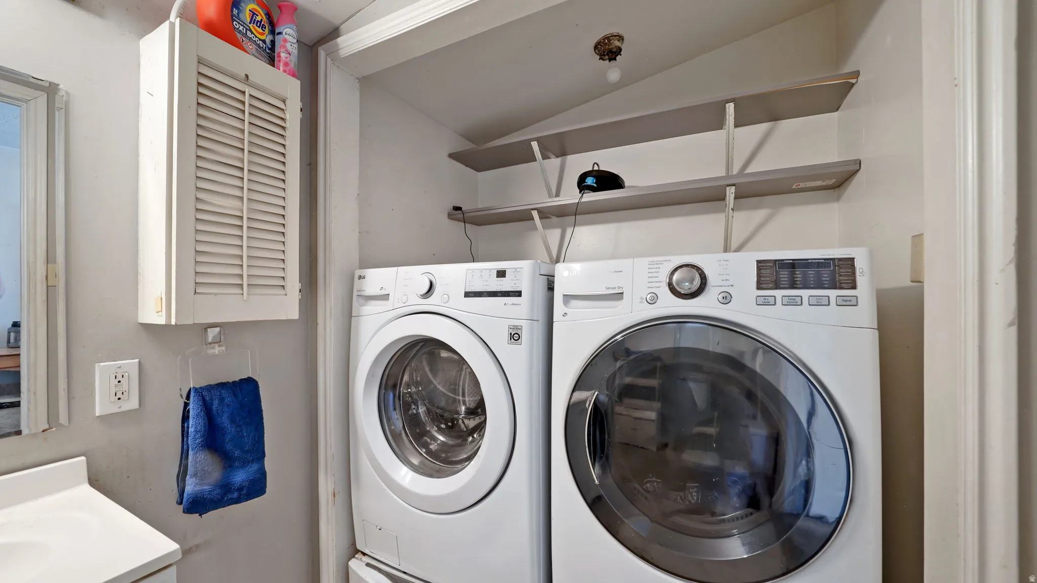 Laundry area featuring a side-by-side washer and dryer, wall-mounted shelving, and a built-in louvered cabinet