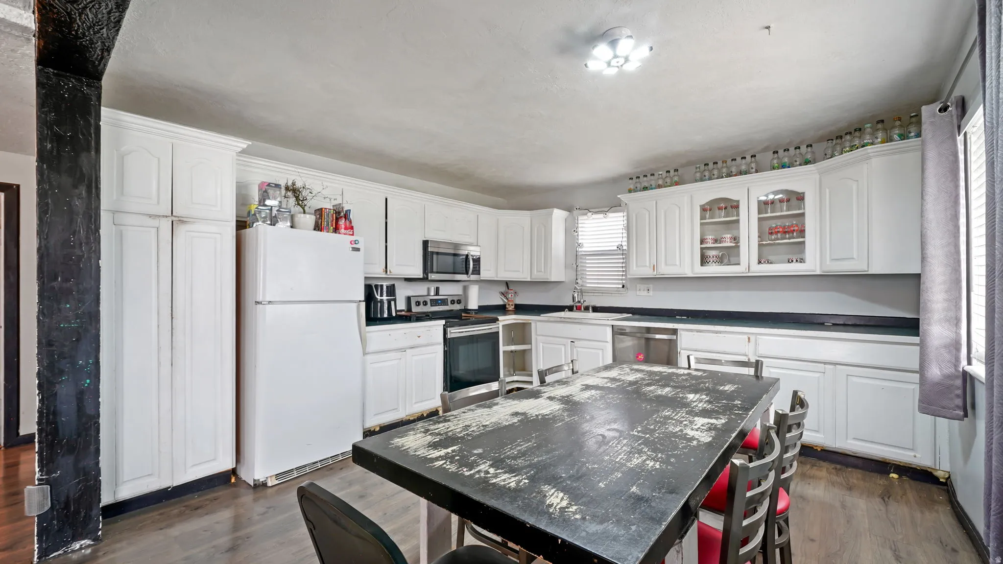 Expansive kitchen featuring wood-finish flooring, white cabinetry, dark countertops, and stainless steel appliances