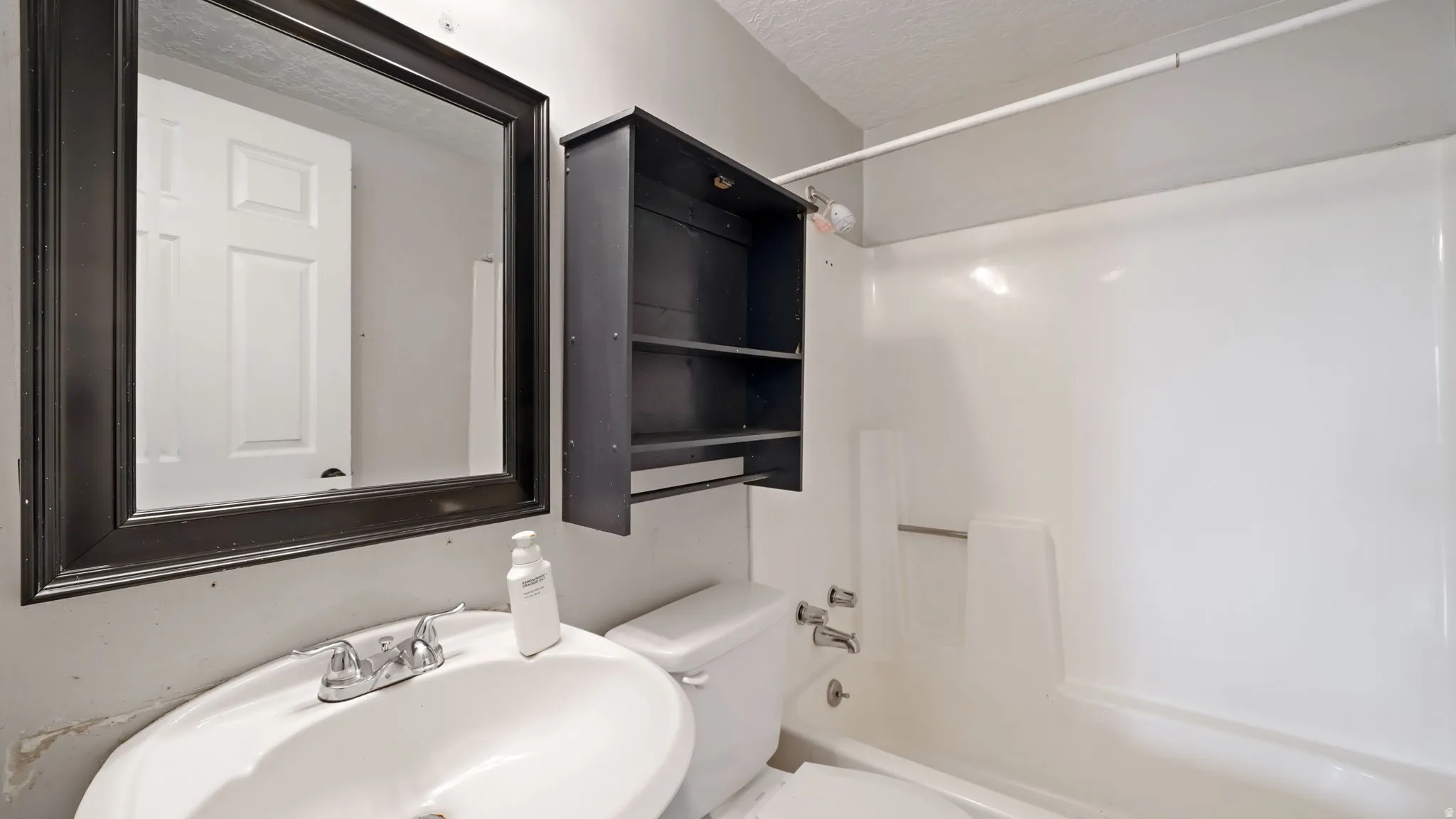 Main bathroom featuring a white ceramic sink with a dual-handle faucet, a framed mirror, and a wall-mounted storage cabinet