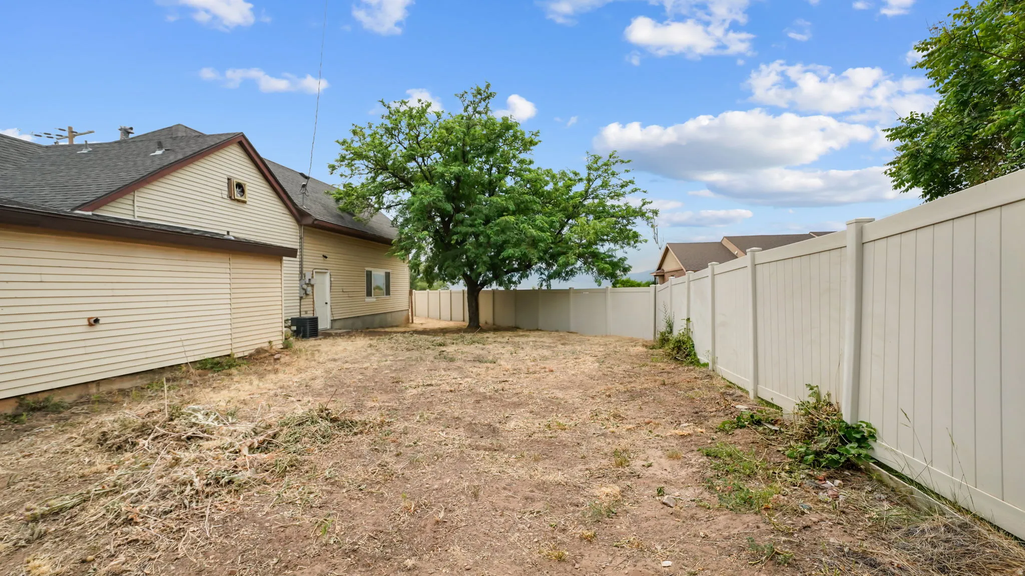 Spacious backyard featuring a substantial mature tree, a full perimeter privacy fence, and a neutral-toned vinyl siding exterior