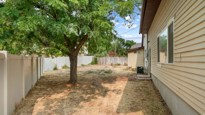 Expansive side yard featuring a mature tree, white privacy fencing, and wood-finish siding