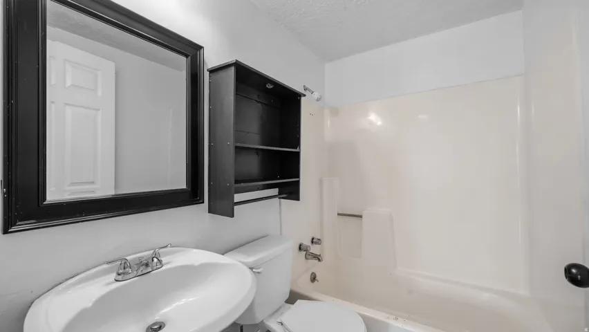 Bathroom with a wall-mounted mirror, built-in shelving, white toilet, and a white sink with a chrome faucet