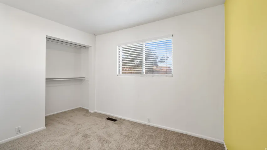 Wall-to-wall carpeting, window with blinds, built-in closet storage, and neutral paint palette