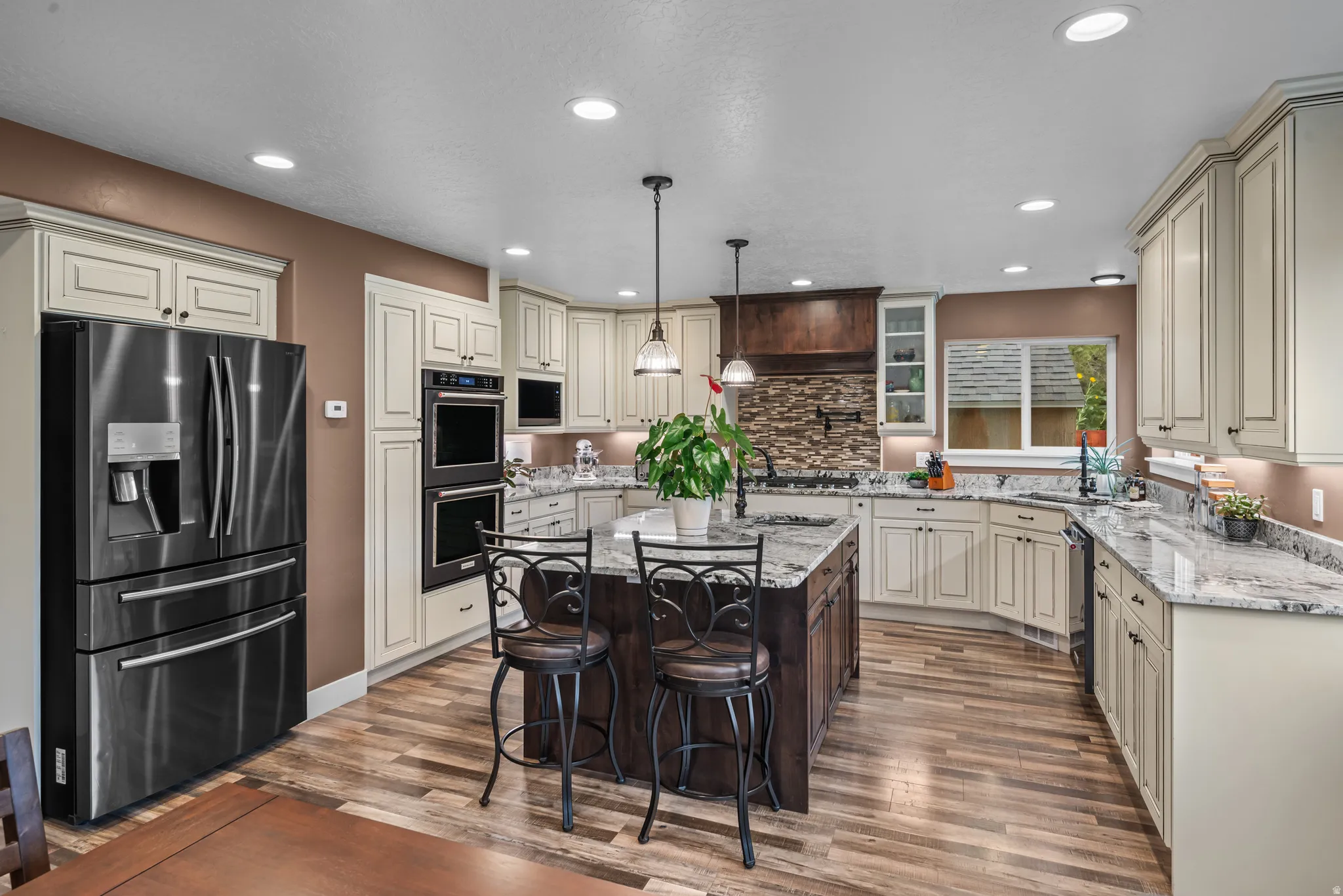 Spacious kitchen featuring a central island with countertop seating, wood-finish flooring, recessed lighting, double wall ovens, and cream-colored cabinetry