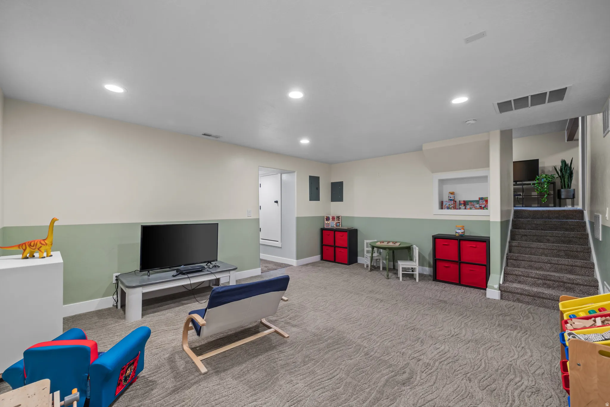 Spacious finished room with recessed lighting, two-tone wall paint, and durable carpet flooring, featuring a built-in display niche and carpeted stairs