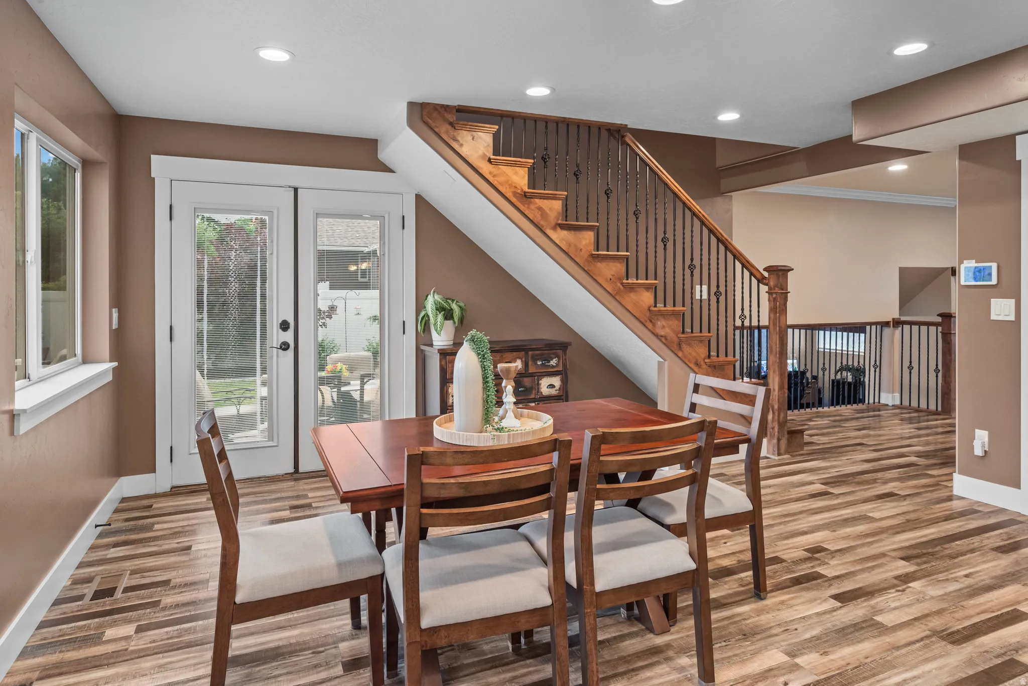 Open-concept space featuring wood-finish flooring, a prominent staircase with iron balusters, recessed lighting, and double glass-paned doors leading to the exterior