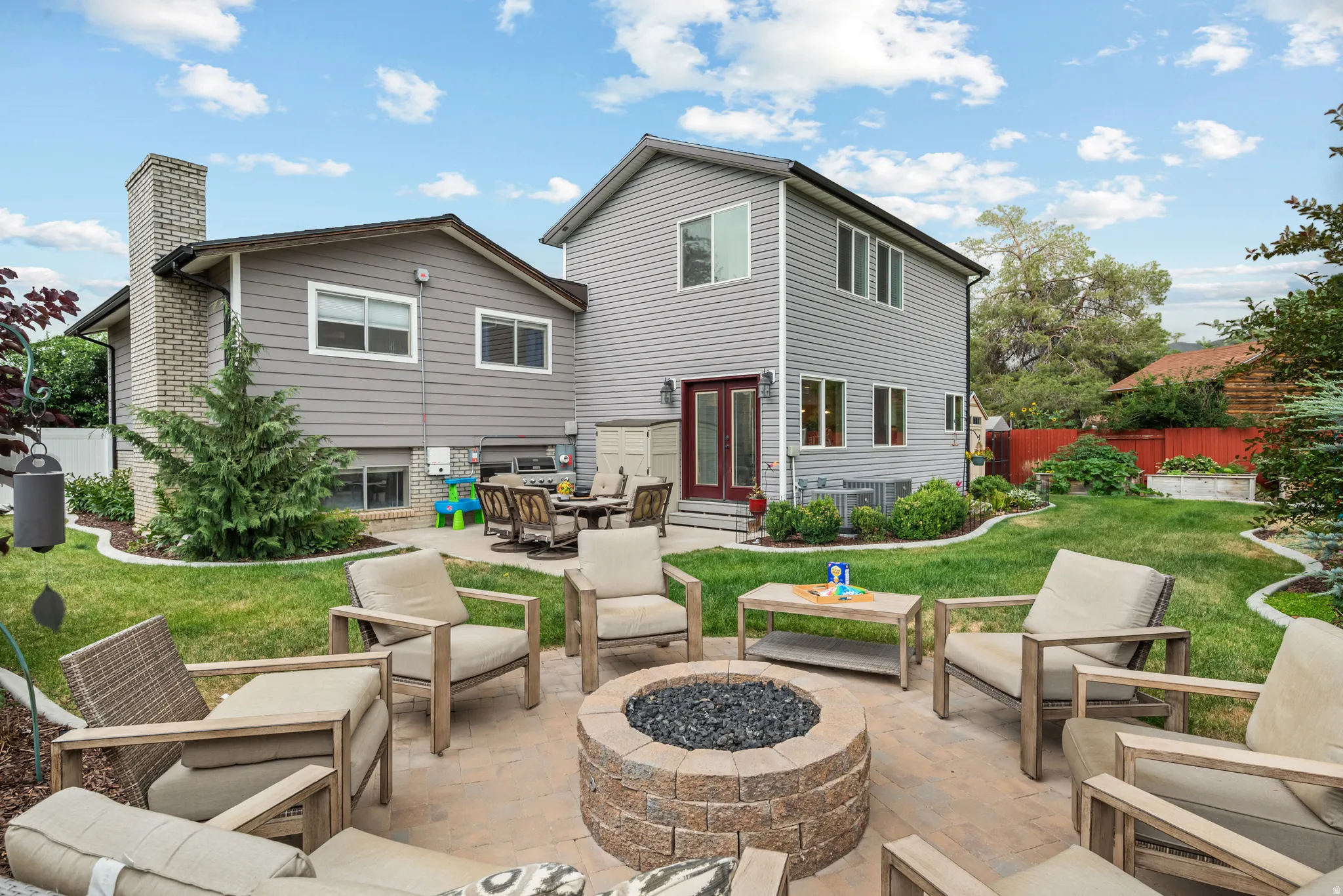 Manicured backyard featuring a paver patio with a built-in fire pit, lush green lawn, and mature landscaping