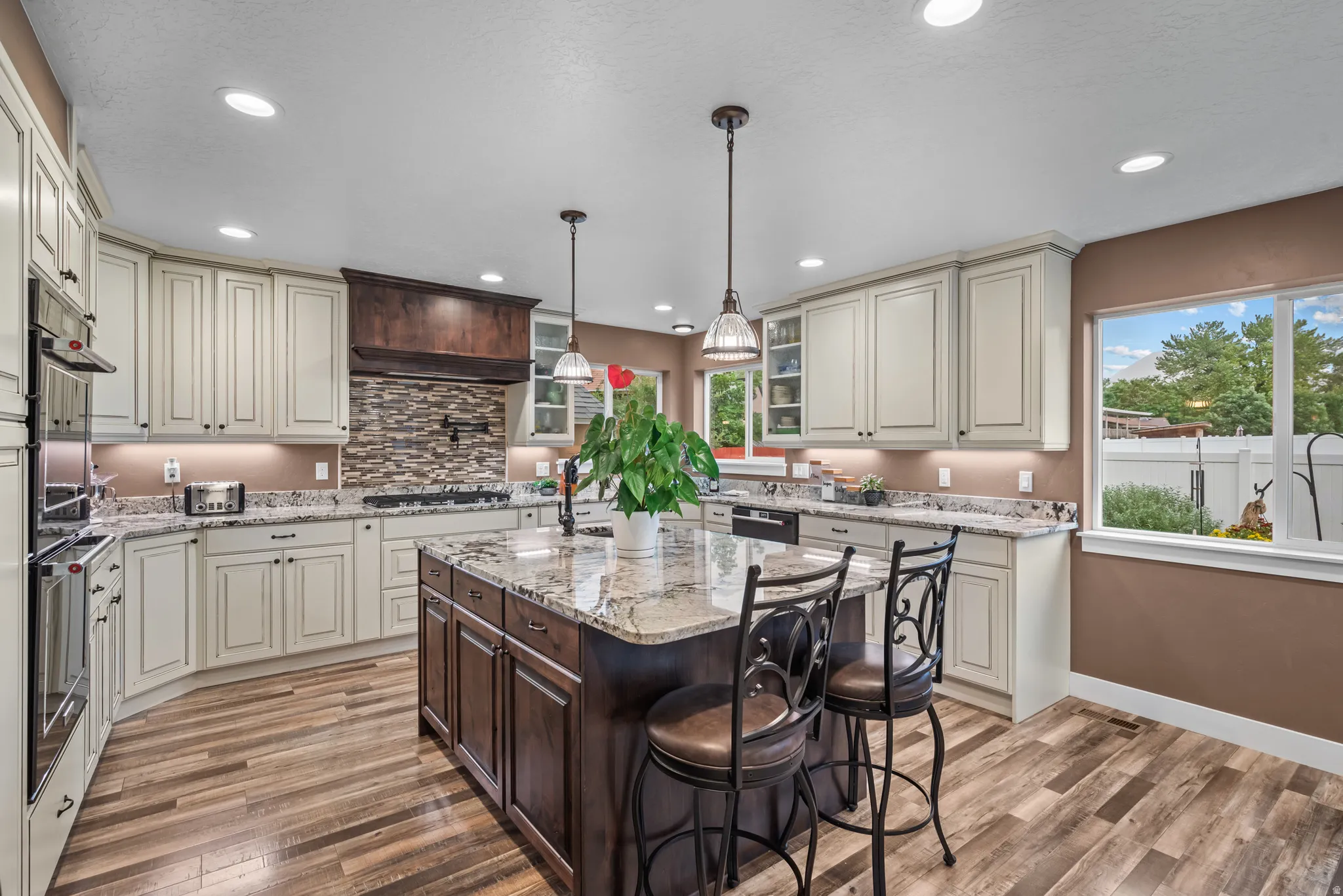 Spacious kitchen featuring an expansive center island with seating, cream-colored cabinetry, stone countertops, integrated stainless steel appliances, and wood-finish flooring