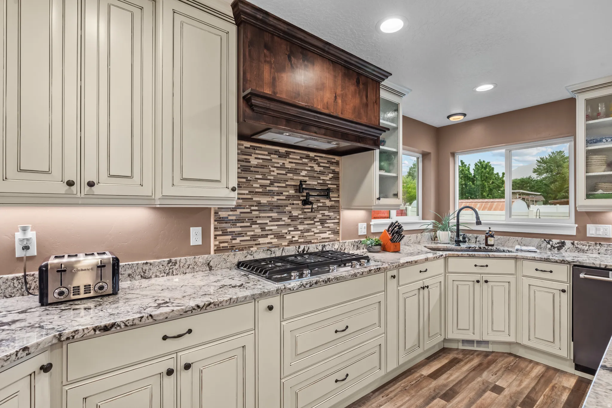 Gourmet kitchen featuring an integrated gas range, granite countertops, decorative tile backsplash, undermount sink, and wood-finish flooring