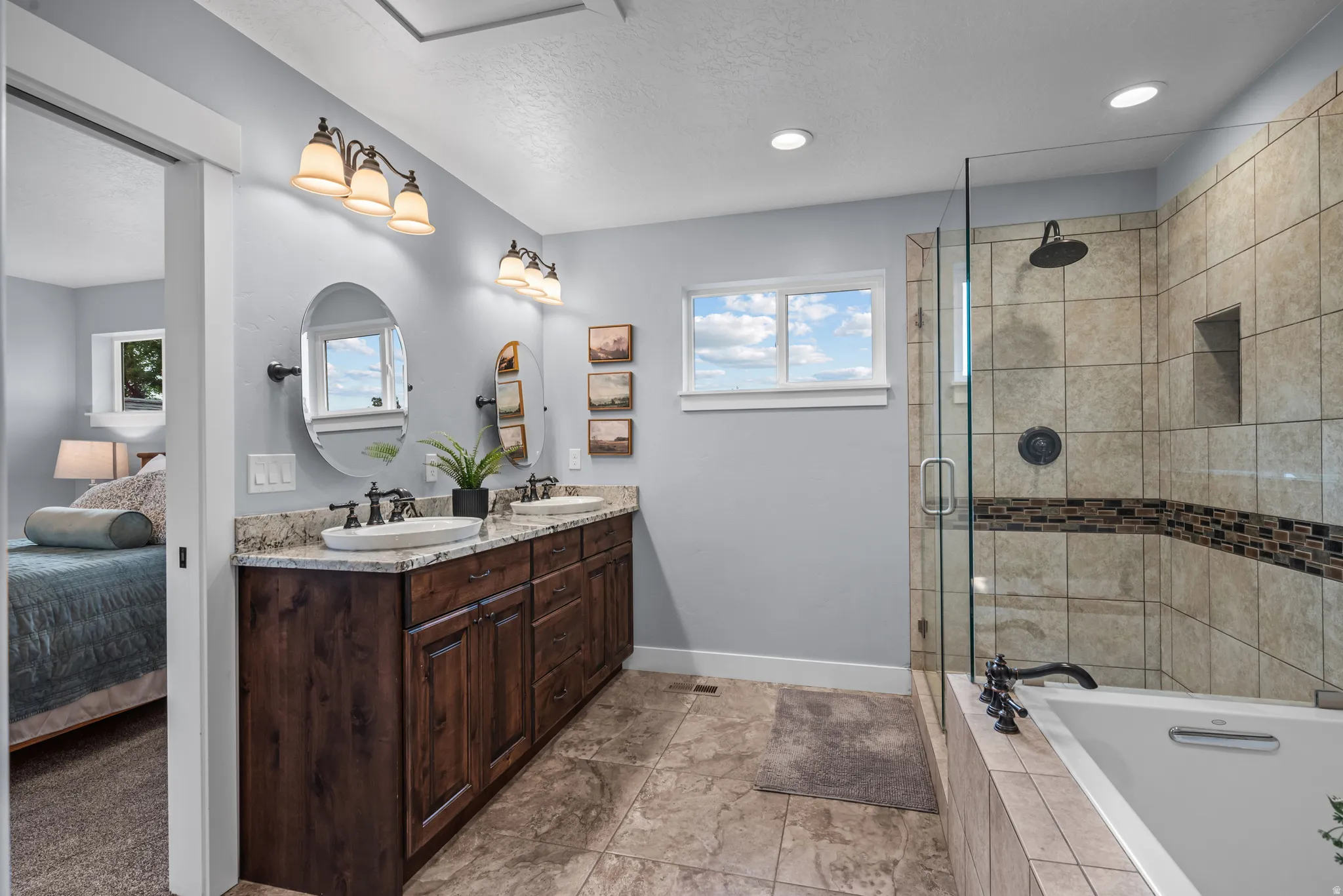 Bathroom featuring a dual vanity with a stone countertop, a glass-enclosed shower with tile surround and an integrated niche, a soaking tub, and tile flooring
