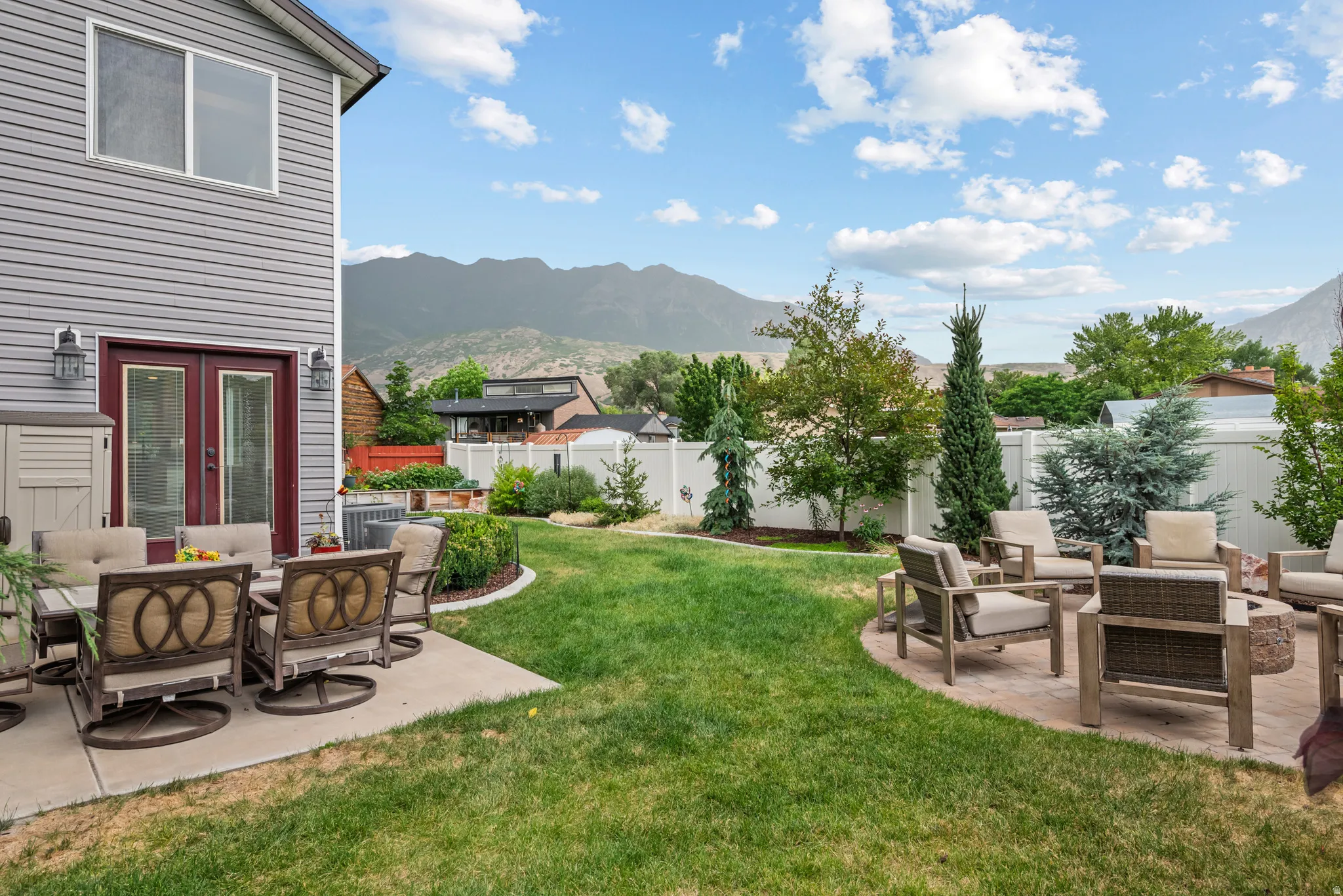 Expansive backyard featuring a lush lawn, two distinct patio areas, mature trees, and a white privacy fence