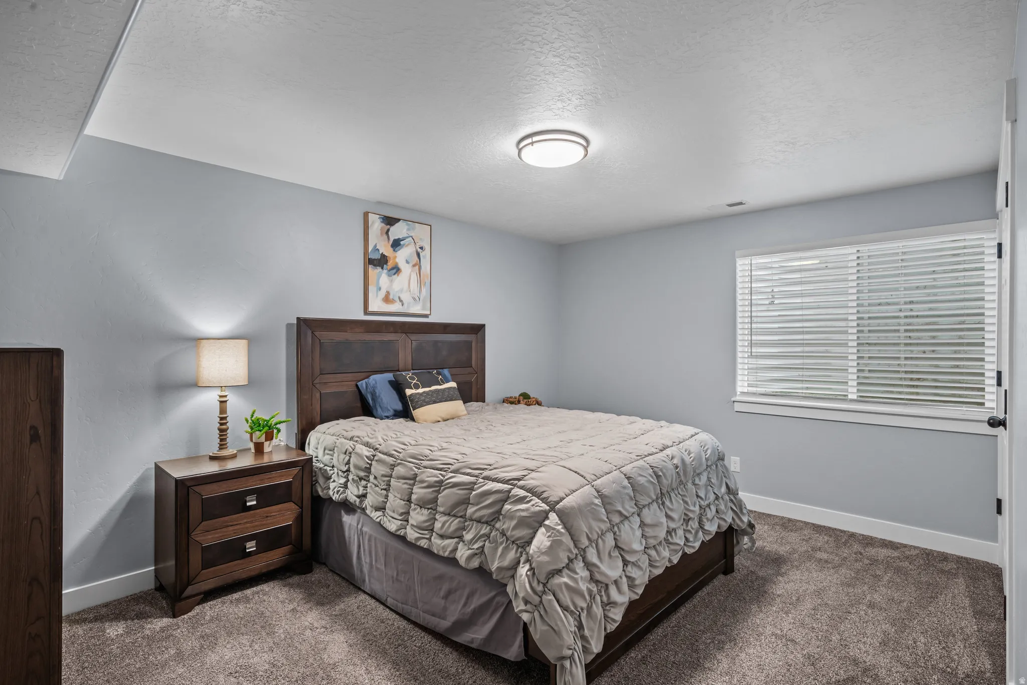 Carpeted interior space featuring a window with white blinds, light gray wall paint, white trim, and a ceiling-mounted flush light fixture